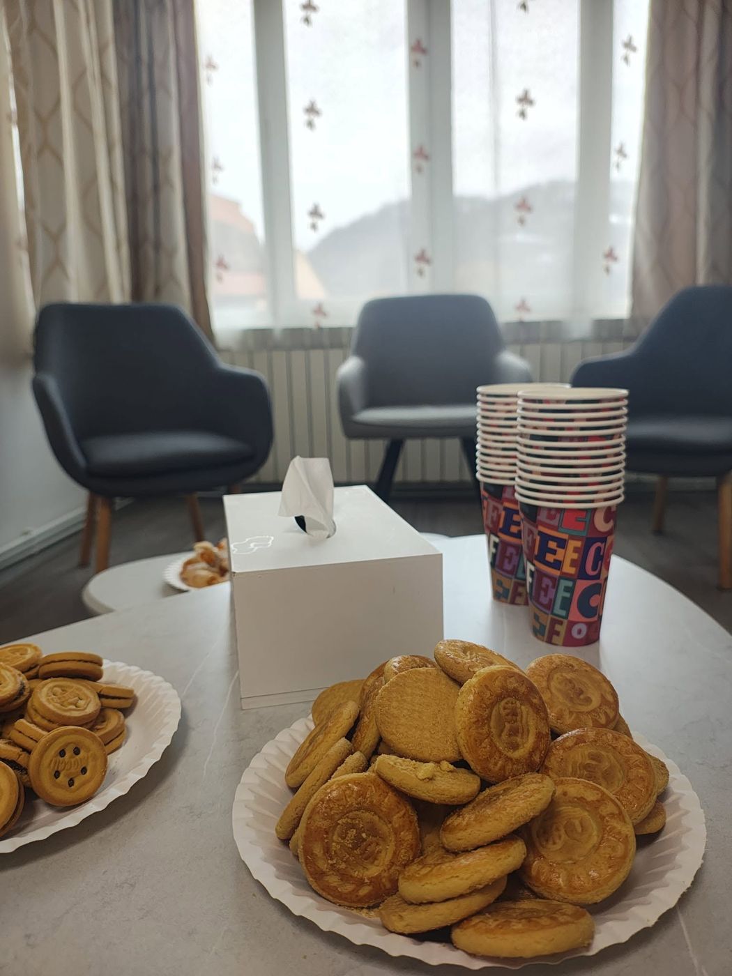 Masă pregătită cu biscuiți și pahare pentru un atelier, cu fotolii în fundal